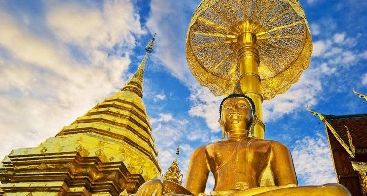 Statue dorée de Bouddha avec un grand parasol doré sur fond de ciel bleu.