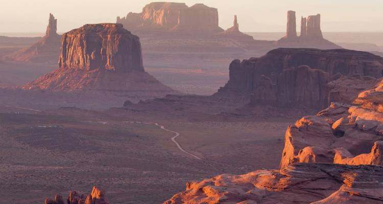 Iconic mesas and buttes of Monument Valley glowing in warm sunrise tones.