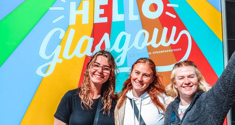Tres mujeres tomándose una selfie frente a una pared colorida en Glasgow.