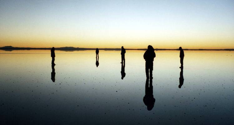 Siluetas de personas en la superficie reflectante del Salar de Uyuni al amanecer.