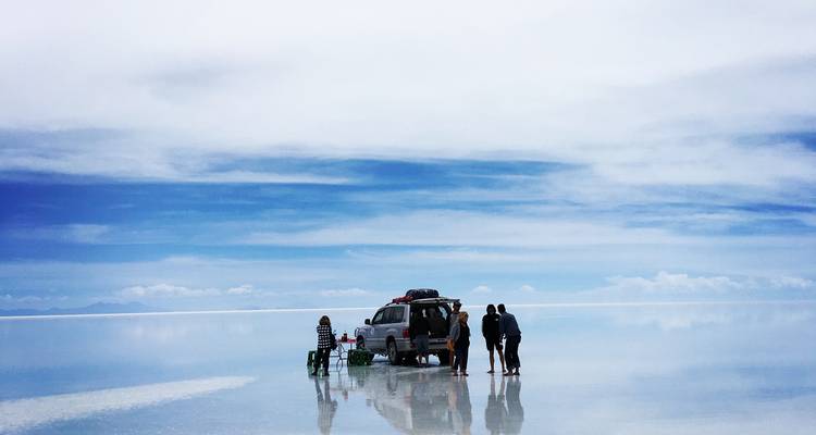 Personas haciendo pícnic con un vehículo sobre la superficie reflectante del Salar de Uyuni.