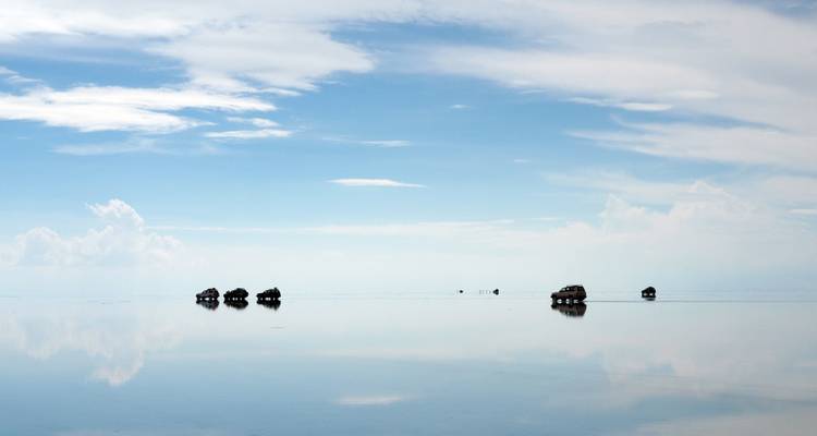 Vehículos conduciendo sobre la superficie reflectante infinita del Salar de Uyuni.
