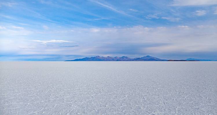 Vasto paisaje plano del Salar de Uyuni con montañas distantes.