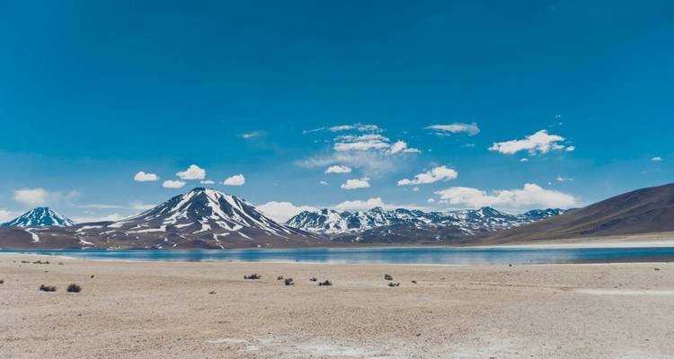 Lagon d'altitude et volcan aux traces de neige sous un vaste ciel bleu sur le plateau de l'Atacama.