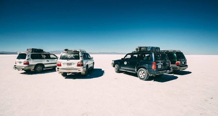 Trois véhicules 4x4 garés sur la croûte blanche infinie des salines sous un ciel dégagé.