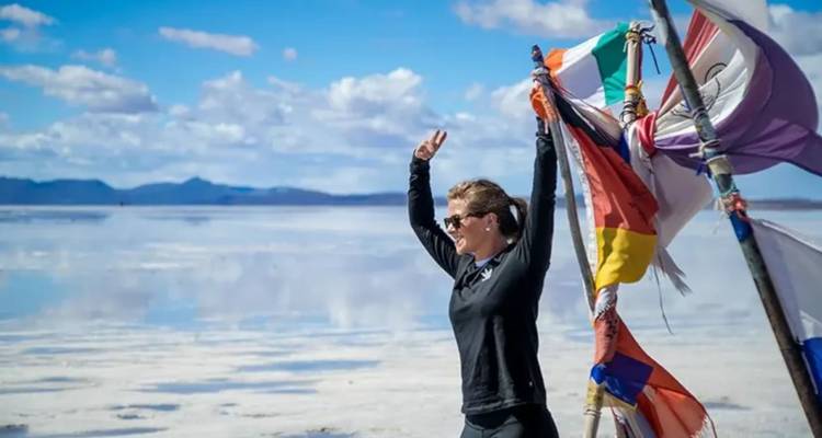 Una mujer posando con banderas coloridas bajo un cielo brillante en salares.