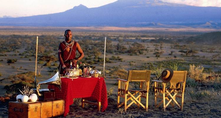 Een man in traditionele kleding bij een versierde tafel met een berg op de achtergrond.