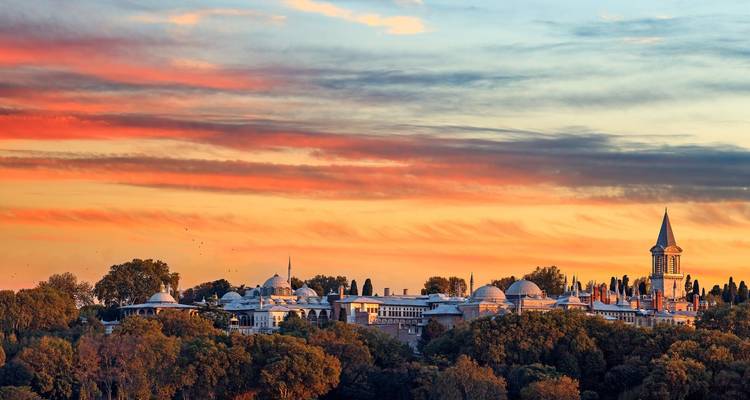 Historischer Palastkomplex umgeben von Bäumen mit einem farbenfrohen Himmel.