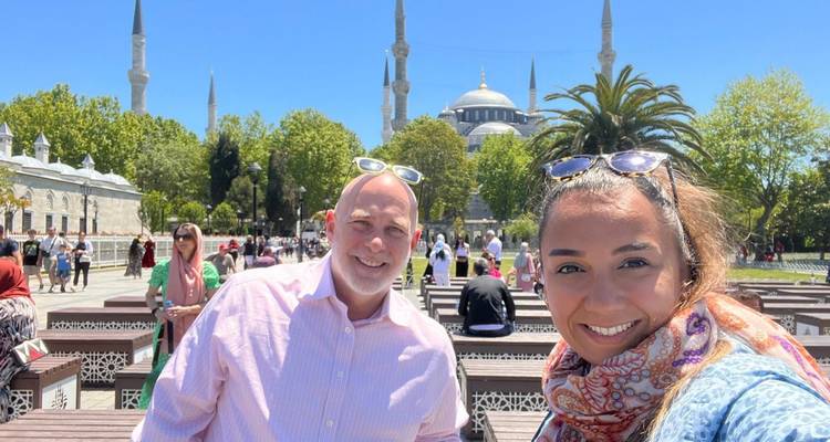 Zwei Personen machen ein Selfie mit einer Moschee und Minaretten im Hintergrund.