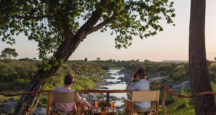 Deux personnes assises au bord d'une rivière avec des boissons.