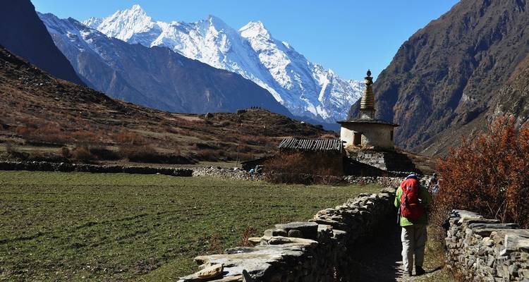 Reisender mit einem Rucksack, der auf einem Steinweg zu einer Stupa in einer Berglandschaft wandert.
