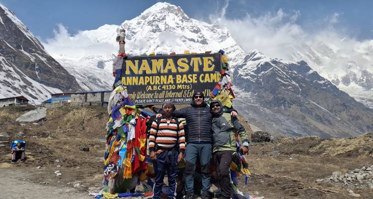Trois personnes posent avec un panneau au camp de base de l'Annapurna.