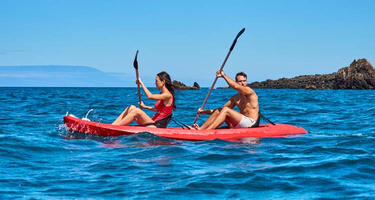 Pareja haciendo kayak en aguas abiertas con islas distantes.
