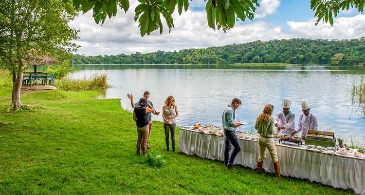 Petit-déjeuner de brousse étalé au bord d'un lac de cratère tranquille tandis que les invités et les chefs discutent sur l'herbe