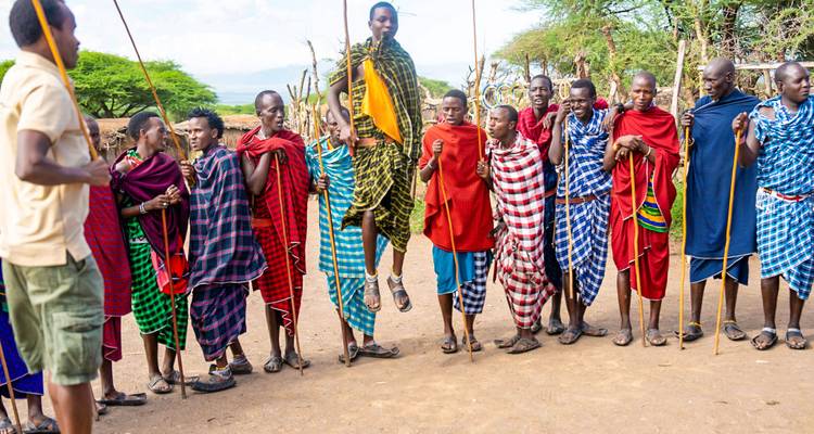 Des guerriers masaï en shukas colorés exécutent une danse sautée dans la clairière de leur village