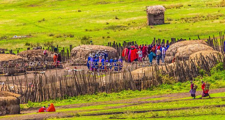 Un boma maasaï traditionnel avec des huttes circulaires enduites de bouse et des villageois rassemblés à l'intérieur d'une palissade sur les plaines vertes