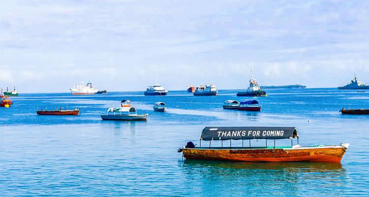 Numerous boats float on turquoise coastal waters; a small wooden boat reads 'THANKS FOR COMING'.