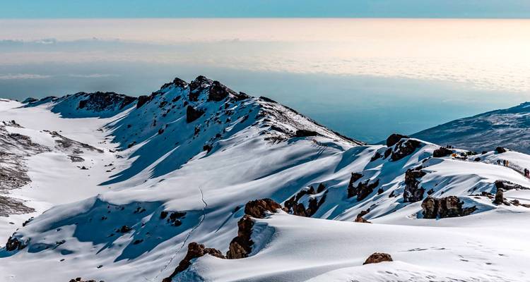 Línea de cresta escarpada y cubierta de nieve muy por encima de las nubes con horizonte distante.
