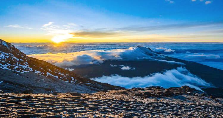 Amanecer dorado sobre un valle lleno de nubes desde una ladera volcánica alta.