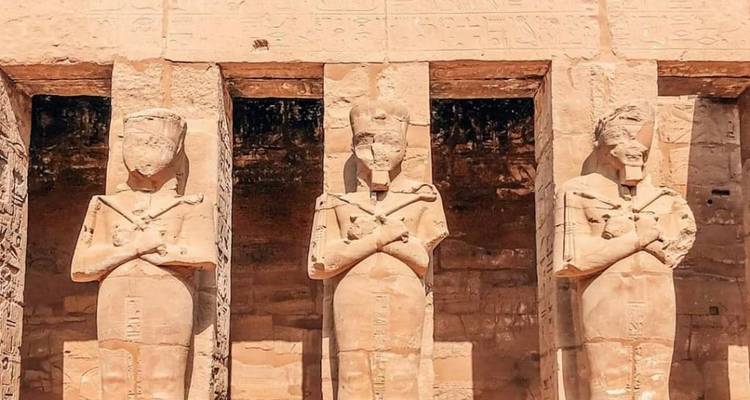 Drei Steinstatuen vor einem antiken Tempel.