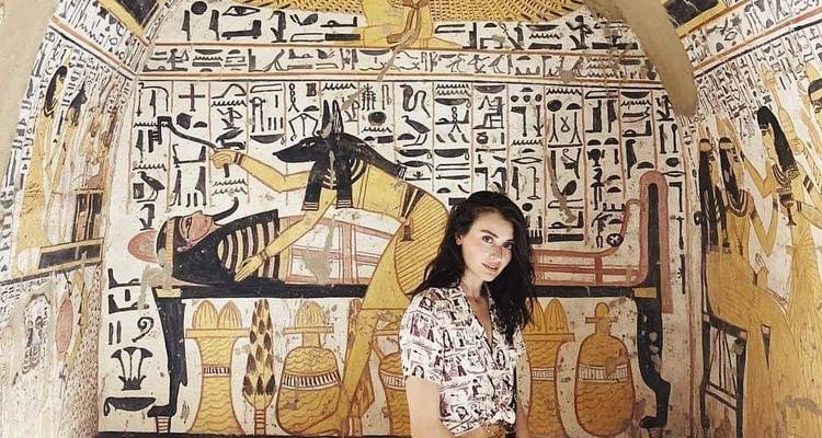 Une femme debout devant un mur avec des hiéroglyphes complexes.