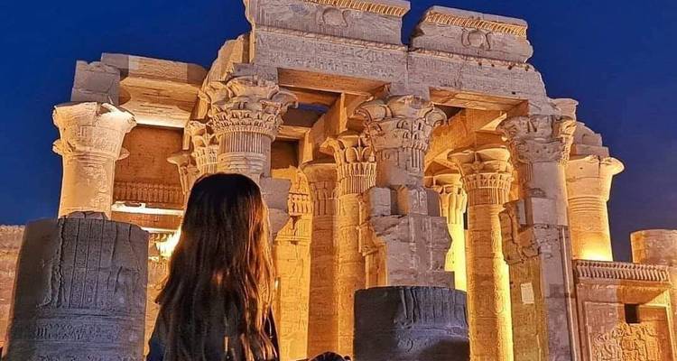 Une femme devant des colonnes antiques illuminées la nuit.