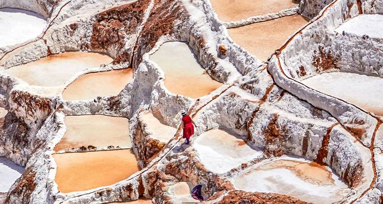 Een persoon die door terrasvormige zoutpannen met verschillende kleuren loopt.