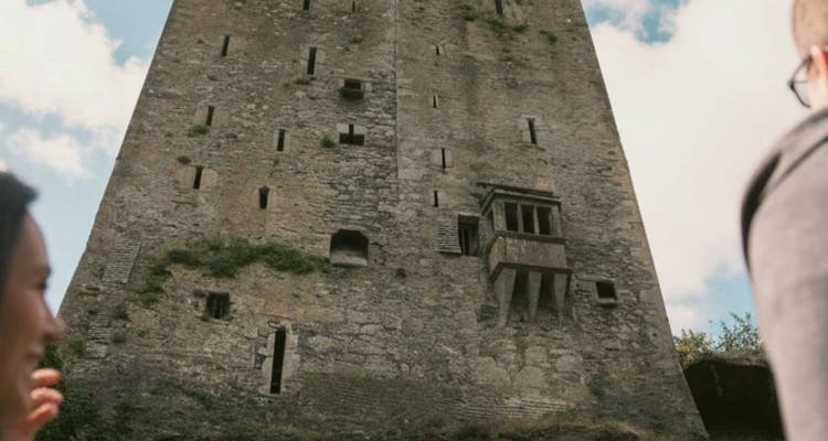 Vue ascendante d'une tour de château de pierre rustique avec des voyageurs qui observent.