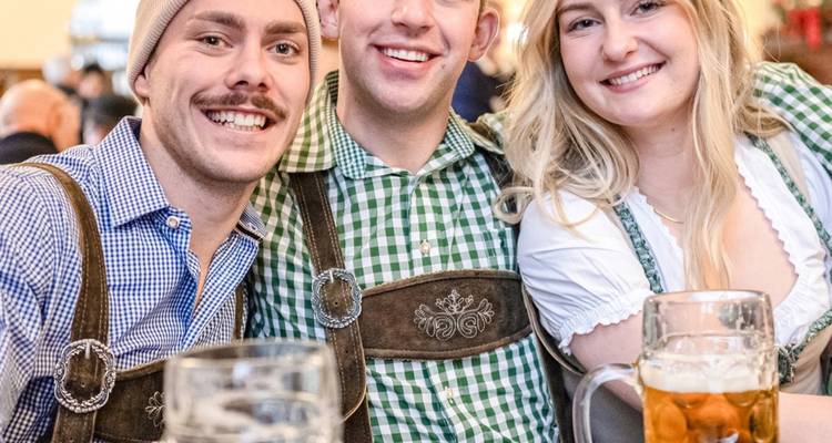 Tres amigos en lederhosen sonriendo con jarras de cerveza llenas en una cervecería de Múnich.