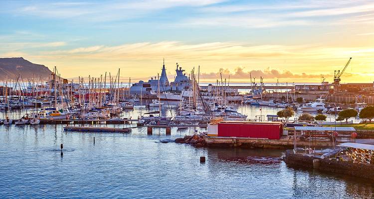 Marina met verschillende boten en een schip bij zonsondergang.