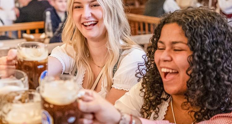 Amigos en traje tradicional brindando con grandes jarras de cerveza dentro de una cervecería bávara.