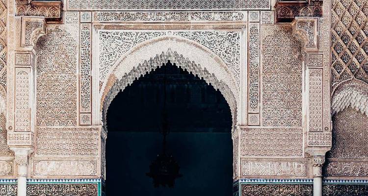 Arco morisco tallado con intricados detalles en estuco y azulejos geométricos que enmarcan un pasillo oscuro.