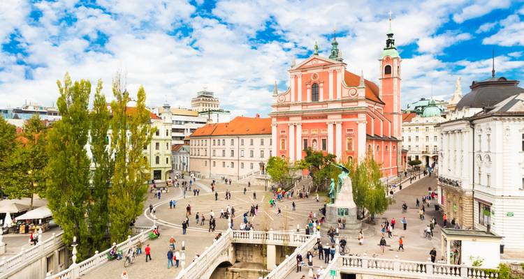 Historische rosa Kirche und Platz in Ljubljana mit gehenden Menschen.