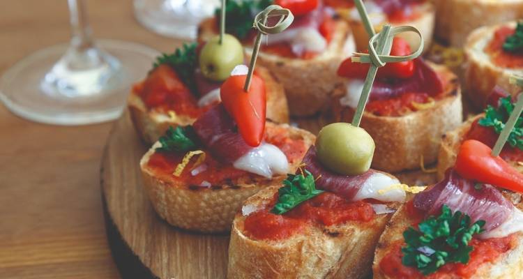 Tapas with wine glasses on a wooden platter.