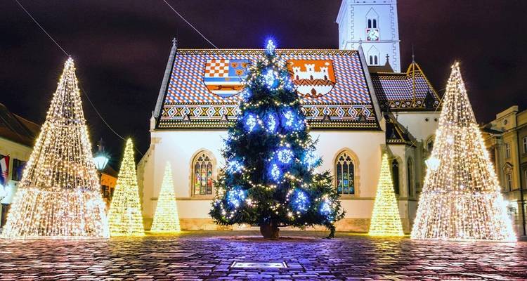L'église Saint-Marc à Zagreb brille la nuit avec des arbres festifs et son toit aux tuiles colorées.