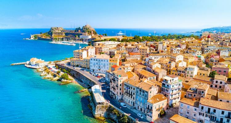 Aerial view of a coastal city with terracotta rooftops and a fortress by the sea.