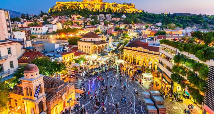 Vibrant cityscape with a lit acropolis and a crowded plaza at dusk.