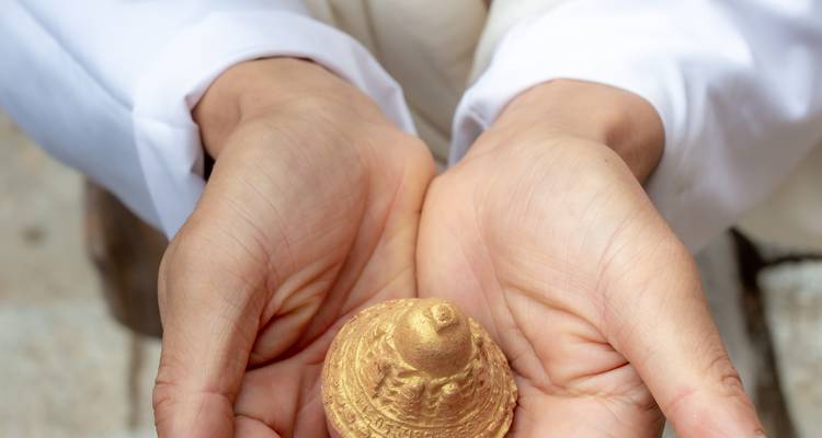 Hands holding a small golden ornament.