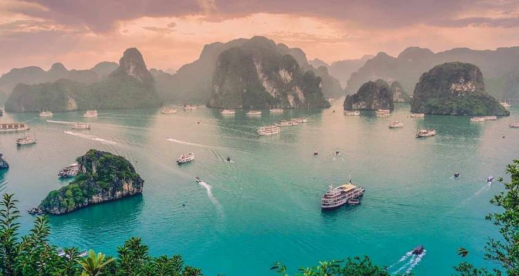 Boats in Halong Bay with limestone islets under a cloudy sky.