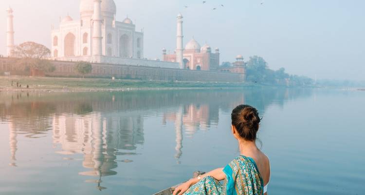 Woman in traditional attire looking at the Taj Mahal across a river.