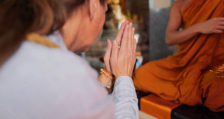 Gros plan d'un voyageur les paumes des mains jointes recevant une bénédiction d'un moine vêtu d'une robe orange.