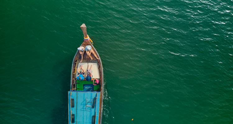 Vue aérienne de haut en bas d'un bateau à longue queue avec des baigneurs dérivant sur une mer vert émeraude.