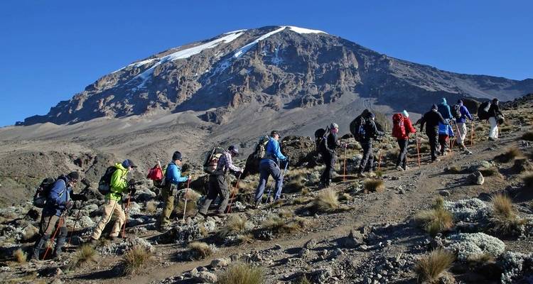 Gruppe von Wanderern, die den Kilimandscharo besteigen, mit schneebedecktem Gipfel in Sicht
