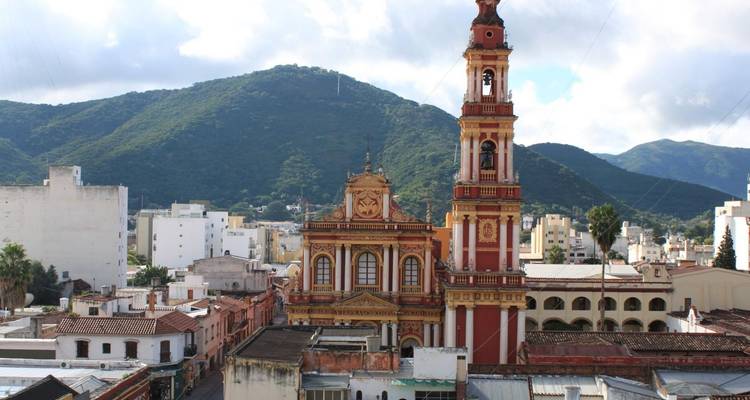 Une cathédrale de style baroque domine un paysage urbain avec des montagnes.