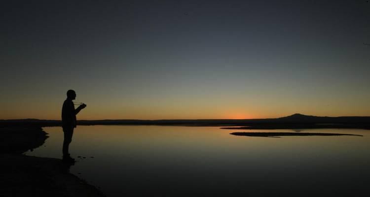Persona de pie junto a un lago al atardecer con silueta oscura.