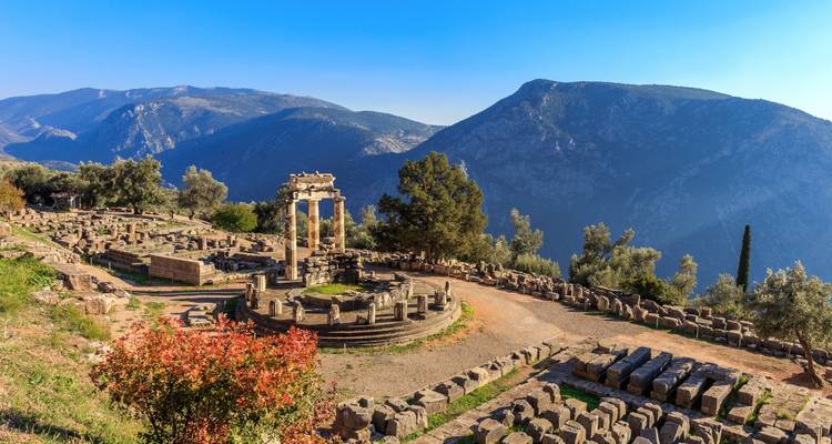 Circular Tholos of Delphi set amidst ancient ruins with sweeping mountain vistas.