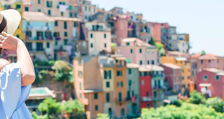 Un voyageur coiffé d'un chapeau de soleil admire les maisons aux couleurs pastel à flanc de falaise des Cinque Terre