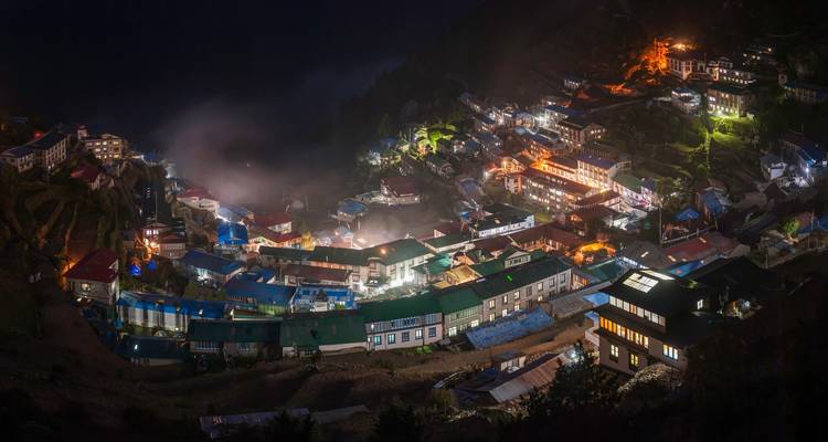 Vue nocturne d'un village avec des lumières illuminant les maisons.