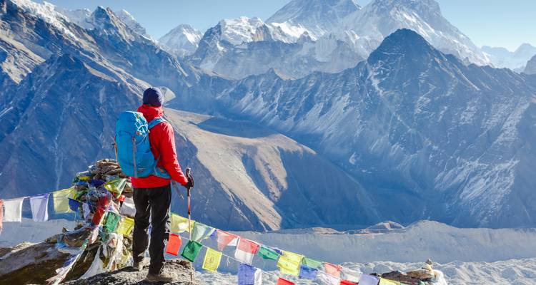 Une personne debout au sommet d'une montagne contemplant les Himalayas enneigées.