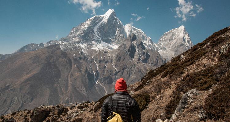 Personne debout sur une colline rocheuse avec des montagnes enneigées en arrière-plan.